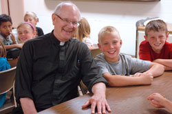 Father Paul Richart poses for a photo with St. Paul Parish Summer Care participants Jonathan Holladay, center, and Luke Lehmenkuler. Father Richart has served as the pastor of St. Paul Parish in Sellersburg for 14 years. He enjoys bringing Communion to elderly parishioners at area hospitals, nursing homes and residences every Wednesday. His mementos from 29 years as an Air Force chaplain include a signed football from the Air Force Academy Falcons, an ice axe used to walk on glaciers in Greenland and folk art from the Philippines. (Photo by Mary Ann Wyand)