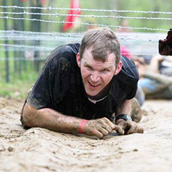 Father Jonathan Meyer crawls beneath barbed wire during the Spartan Race in Laurel on April 27, 2012. The barbed wire challenge will be part of the “Tame the Terrain” race in North Vernon on June 22. The event is a fundraiser to benefit young adults and teenagers who are members of St. Mary Parish in North Vernon, and St. Ann and St. Joseph parishes in Jennings County. (Submitted photo)