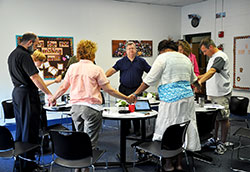 From left to right, St. Monica Parish pastor Father Todd Goodson, Michelle Meer, Christina Dickson (partially obscured), Anne Corcoran, John McShea, Dabrice Bartet, Mary Shepherd and Ed Witulski conclude a meeting in prayer on July 9 at St. Monica Parish in Indianapolis. Through a series of nine novenas, nine holy hours and a prayer service, the group seeks to curb the increasing trend toward deadly violence. (Photo by Natalie Hoefer)