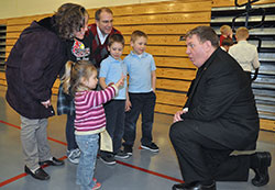 Archbishop Joseph W. Tobin reacts to 3-year-old Kathryn Mack showing him her age during a Feb. 19, 2013, reception at St. Louis Parish in Batesville following a Mass celebrated there by the archbishop for Catholics in the Batesville Deanery. Joining Kathryn in meeting the archbishop are members of her family, from left: Deb, Grace (partially obscured), Pete, Christian and Spencer Mack, all members of St. Louis Parish. (Criterion file photo by Sean Gallagher)