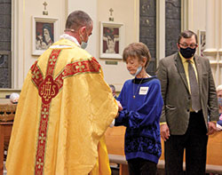 Judy Townsend receives her first Communion from Father Dustin Boehm during the Easter Vigil Mass on April 3 in St. Gabriel Church in Connersville. Her badge bears her confirmation name, St. Abigail. (Submitted photo by Mellissa Ackerman)