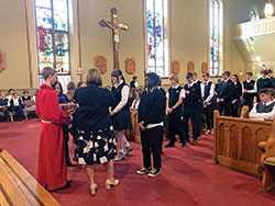 Altar server Zachary Hoff holds a basket of blessed Miraculous Medals as the school’s president Diane Laake (to his left) and principal Angie Parmer (to his right) place a medal around the neck of each new student and staff member on Dec. 8. (Submitted photo by Theresa Murphy)