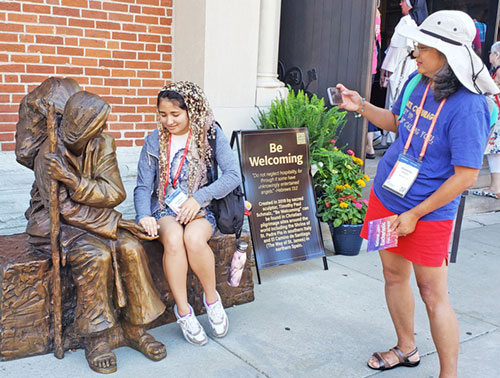 Kimberlie Petrulis, right, takes a photo as her daughter Josephine Petrulis engages with a sculpture called “Be Welcoming” outside St. John the Evangelist Church in Indianapolis on July 18. The two members of the Diocese of Richmond, Va., admired the piece, one of two created by Catholic sculptor Timothy Schmalz for the National Eucharistic Congress. (Photo by Natalie Hoefer)